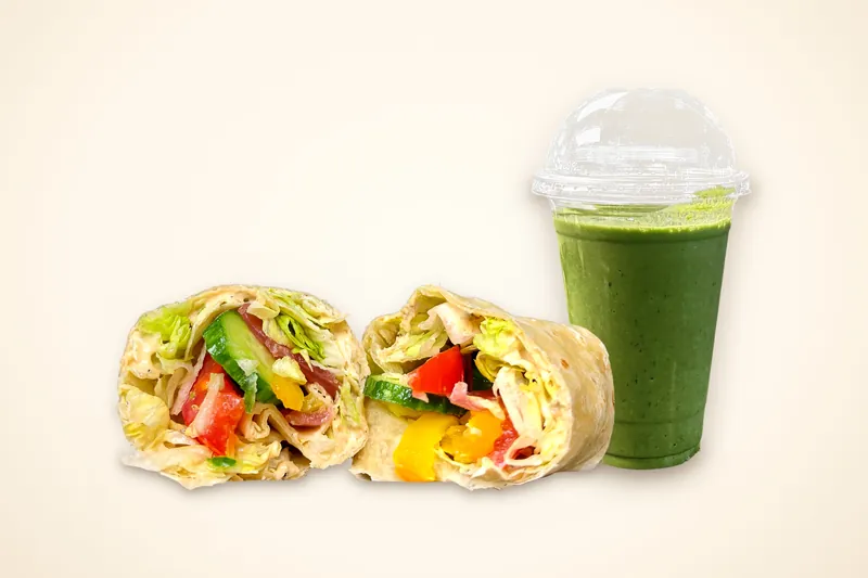 Hummus Wrap + Smoothie Combo: the Hummus Wrap cut in half next to a green Pineapple Mango Green smoothie in a domed cup