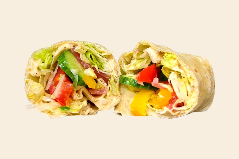 Hummus Wrap in a flour tortilla, cut in half to show hummus, cucumber, tomato and greens